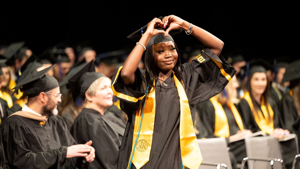 A woman on the stage at Tippie graduation, holding her hands in the shape of a heart.