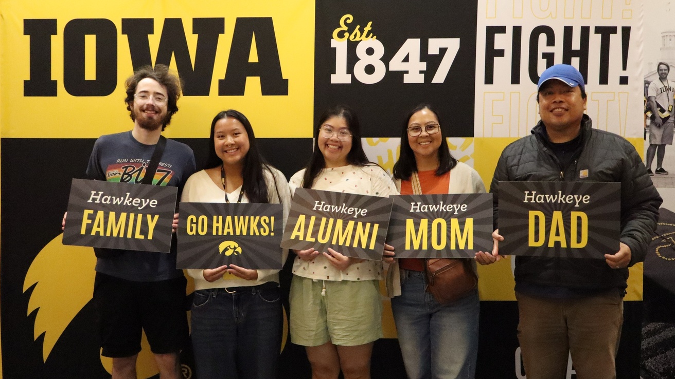 A family posing for a photo at Hawkeye Visit Day, holding black and gold signs.